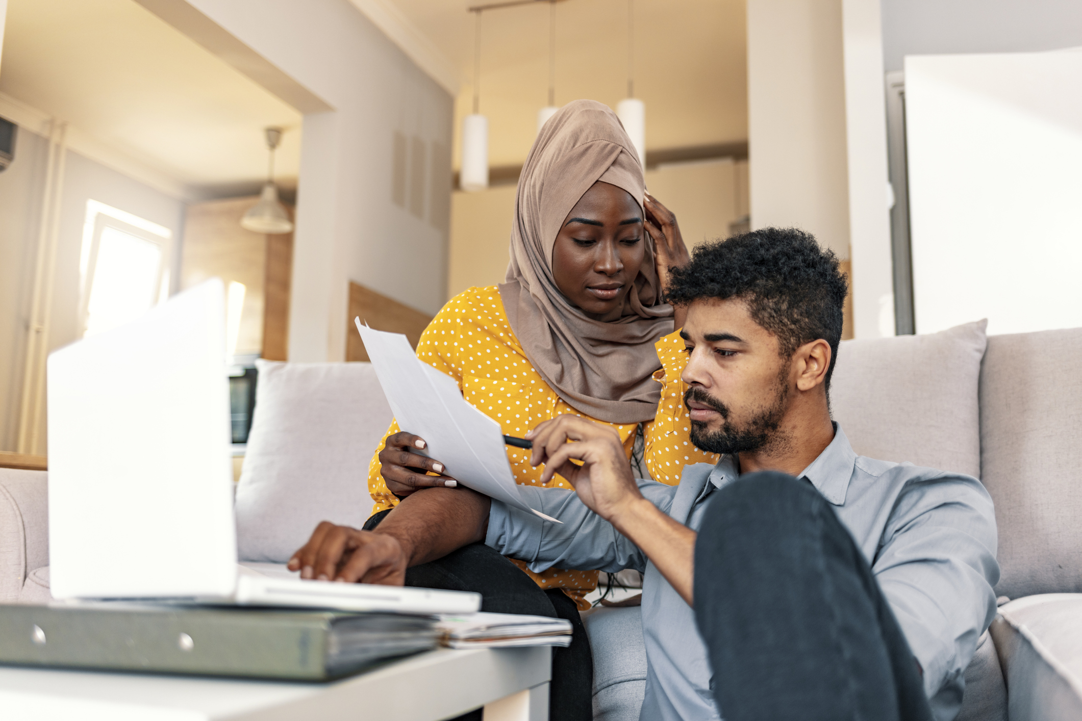 Young muslim African family of two managing finances at home, reviewing bank accounts, sitting with notebook computer. Wife and husband paying taxes online on laptop.